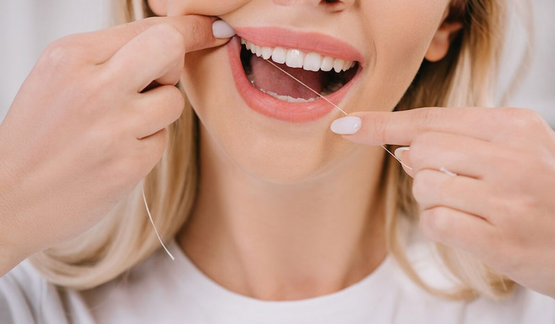 Trồng răng Implant có bị hôi miệng không và cách khắc phục Dùng chỉ nha khoa đưa vào kẽ răng để đẩy thức ăn ra ngoài